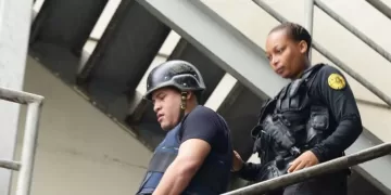 Oficial de la Policía Nacional escolta a Mantequilla con casco y chaleco antibalas por una escalera metálica en un operativo de seguridad.